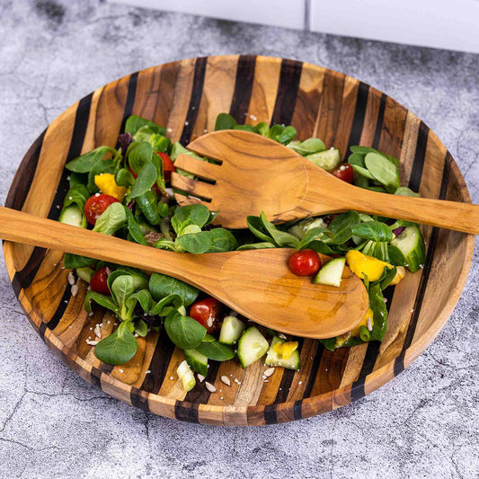 Upcycled wooden salad servers resting on a colorful salad in a wooden bowl